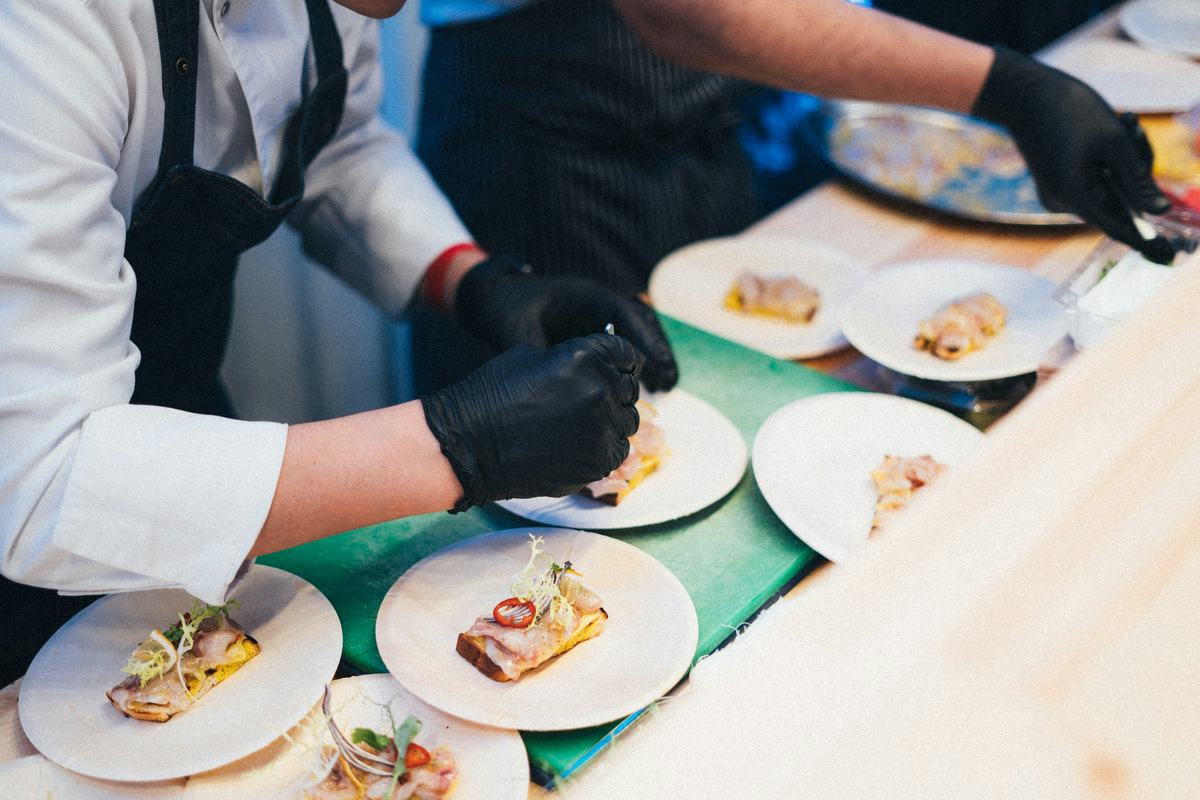 Chefs in gloves plating small portions of food in a commercial kitchen